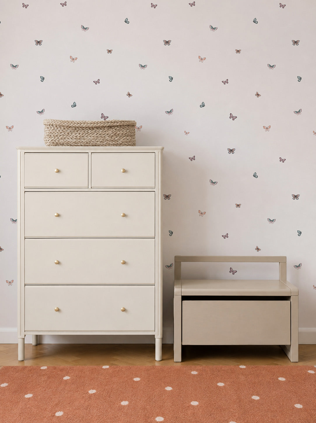 A cream-colored dresser and a small bench sit on a wooden floor. The wall behind is adorned with Bibi Butterflies Wallpaper, featuring a charming hand-drawn butterfly repeat pattern, while an orange rug with white dots is partially visible in the foreground.