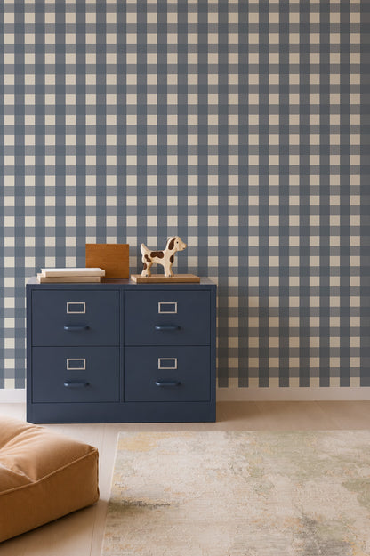 A navy blue four-drawer filing cabinet stands against a wall covered in Large Check Wallpaper, Deep Blue, topped with a wooden dog figurine and books.