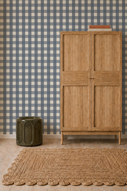 A tall wooden cabinet and a dark green ceramic stool sit in front of Large Check Wallpaper, Deep Blue above a woven rug.
