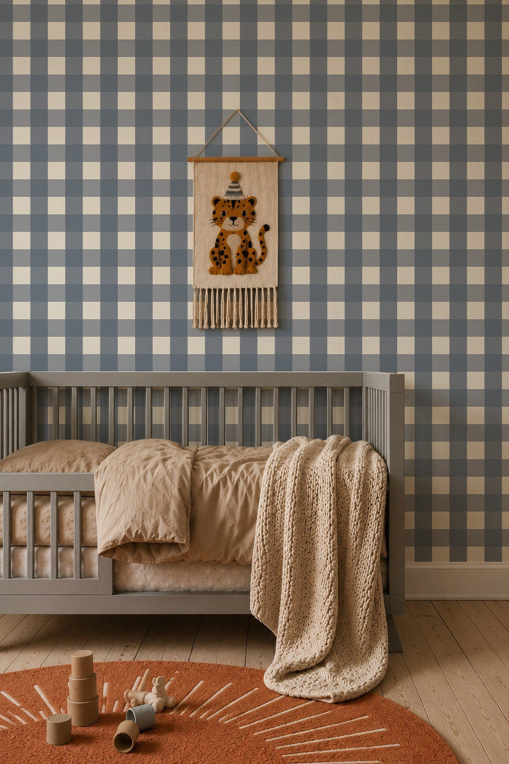 A gray crib with neutral bedding sits in front of Large Check Wallpaper, Deep Blue featuring a decorative wall hanging of a leopard wearing a party hat.