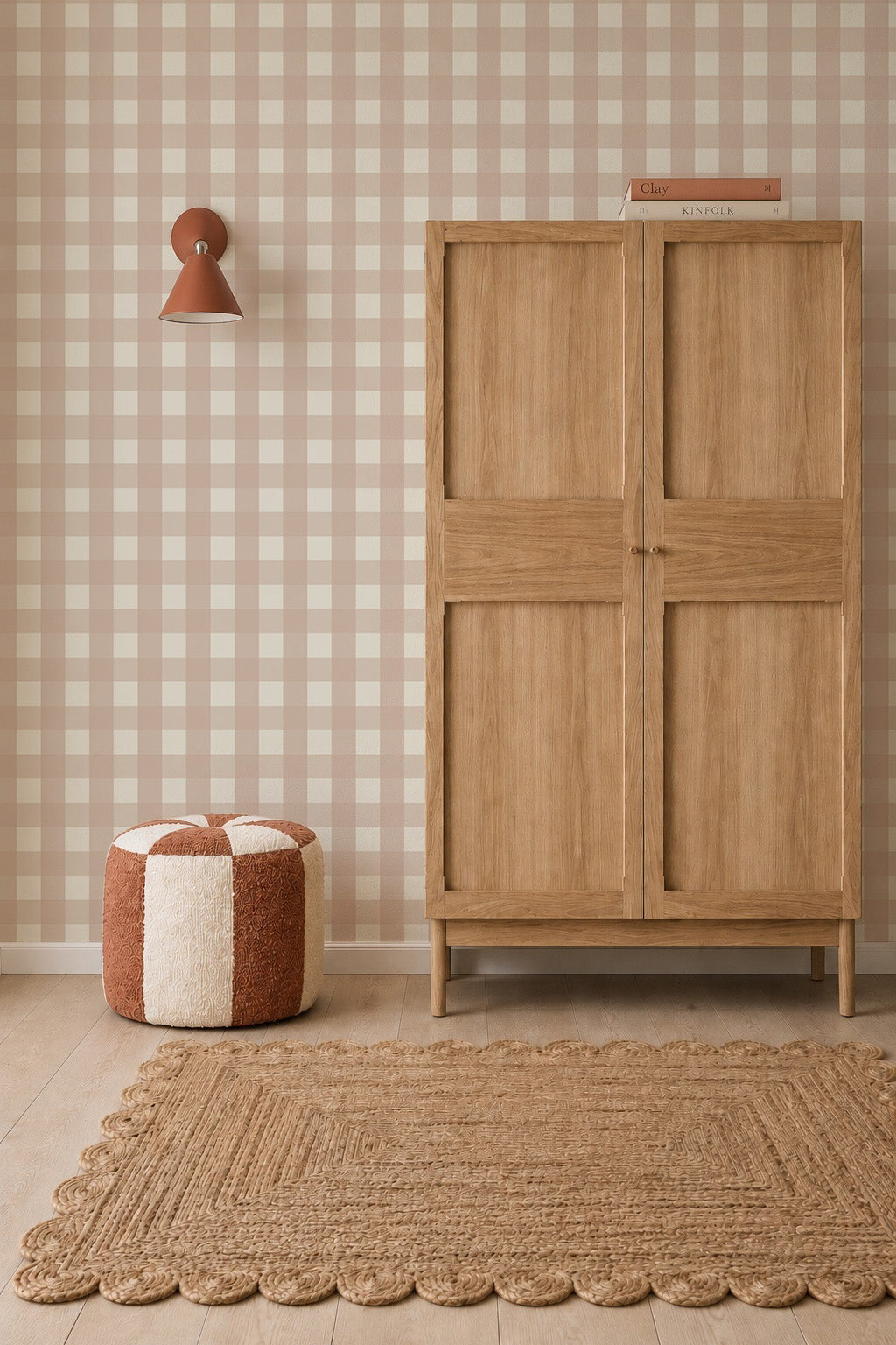 A wooden wardrobe stands against Large Check Wallpaper, Pink nursery wallpaper next to a round pouf and a textured area rug.