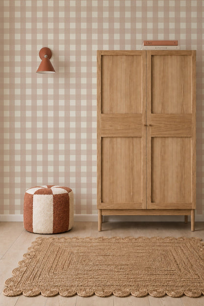 A wooden wardrobe stands against Large Check Wallpaper, Pink nursery wallpaper next to a round pouf and a textured area rug.