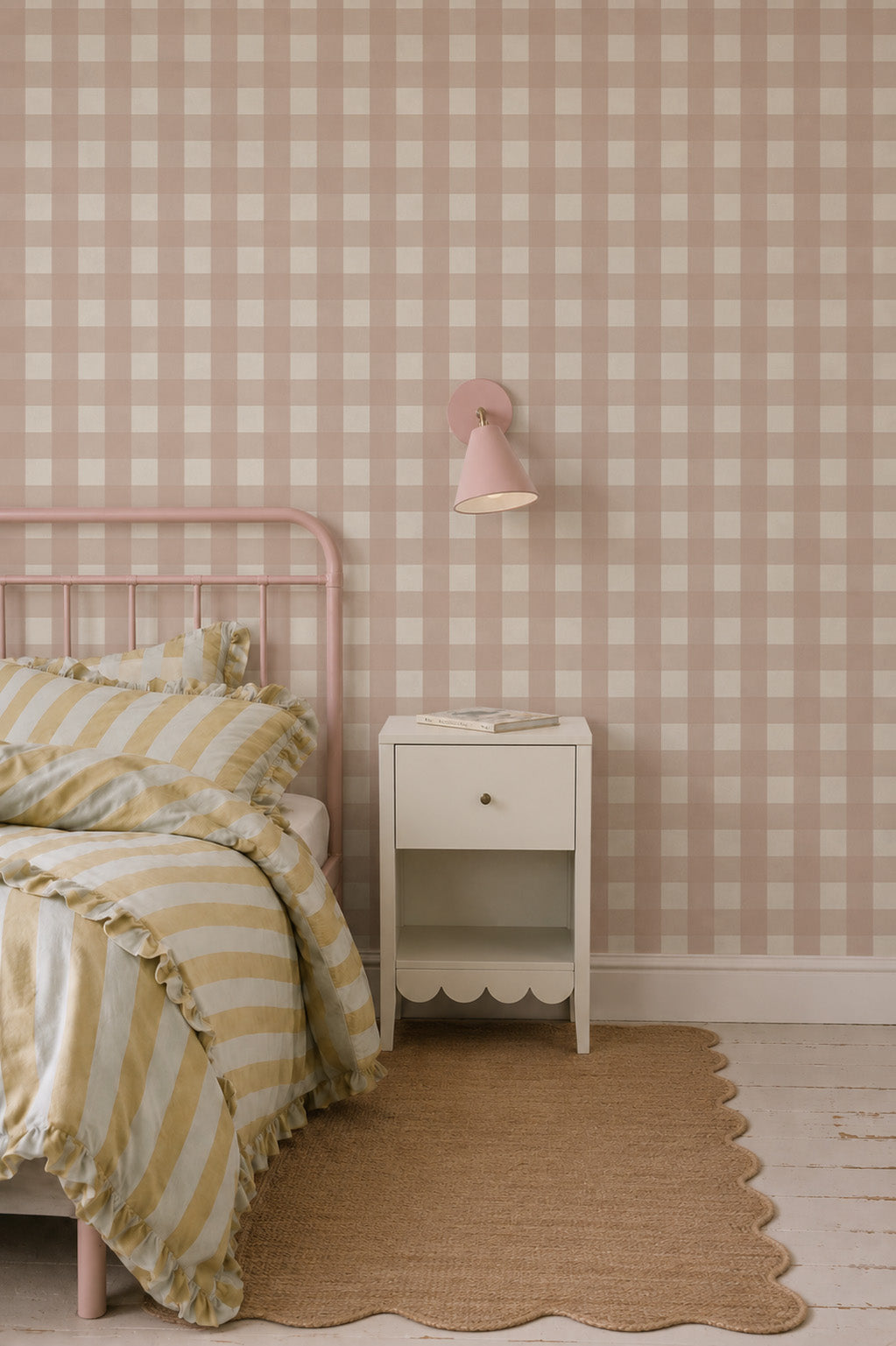 A bedroom featuring a pink metal bed frame, a white bedside table with a scalloped bottom, and Large Check Wallpaper, Pink.