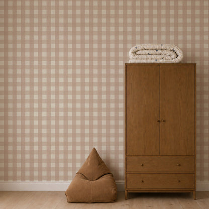 A wooden wardrobe stands against Large Check Wallpaper, Pink, with a folded patterned blanket on top and a brown pyramid-shaped beanbag on the floor.