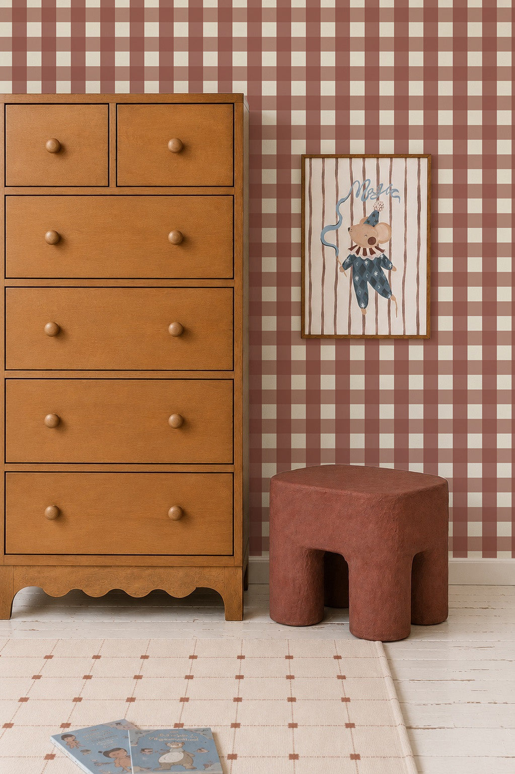 A wooden dresser stands next to a small stool and a framed illustration of a circus mouse on Large Check Wallpaper, Red.
