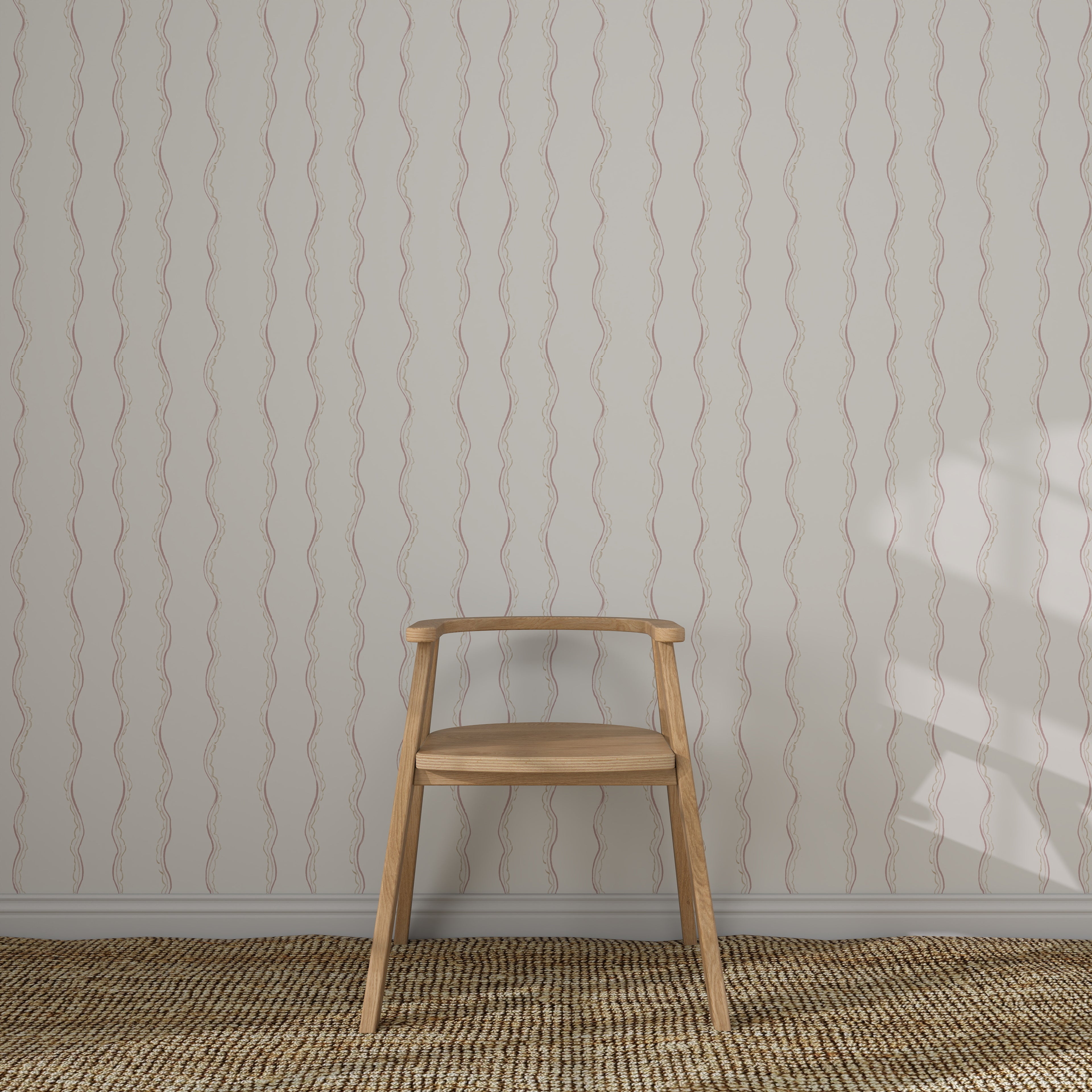 A simple wooden chair sits against a wall adorned with Ribbon Stripe Wallpaper in Rose. The floor features a textured woven rug, and gentle light casts a shadow, creating elegant children&