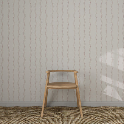 A simple wooden chair sits against a wall adorned with Ribbon Stripe Wallpaper in Rose. The floor features a textured woven rug, and gentle light casts a shadow, creating elegant children&