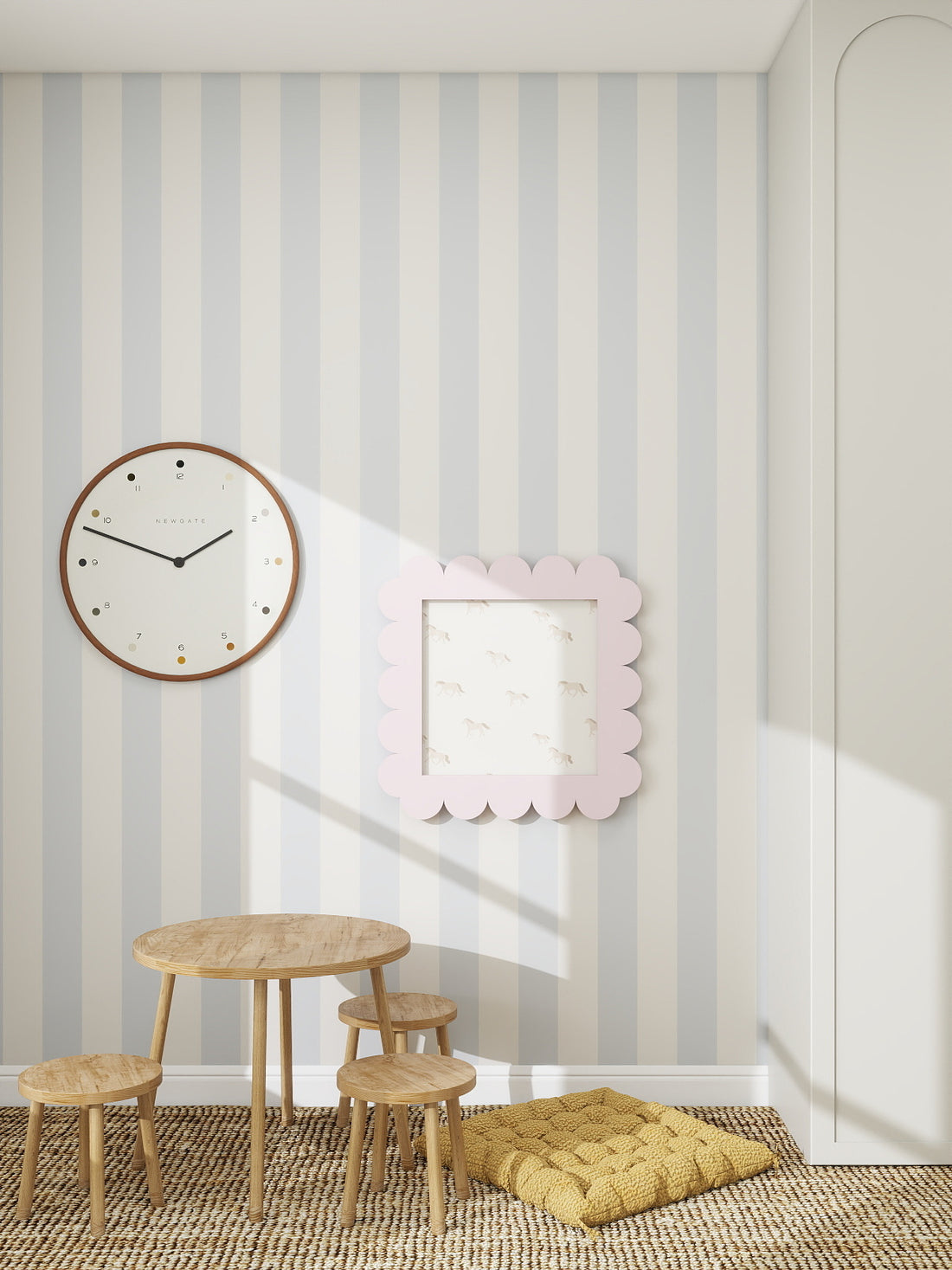 A children’s playroom featuring Circus Stripe Wallpaper Sky in light grey and white, a round wall clock, pink scalloped picture frame, small wooden table and stools, and a yellow floor cushion on a woven rug—perfect for any kids’ space.