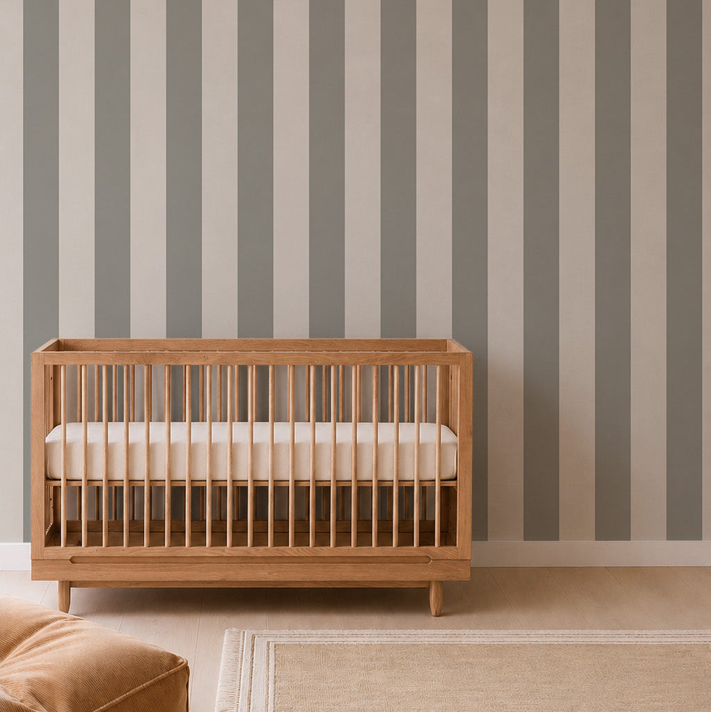 A wooden crib with a white mattress sits in front of the Circus Stripe Wallpaper, Matcha in a nursery with light wood flooring and a beige rug, adding a playful yet elegant touch to the space with this charming nursery wallpaper.