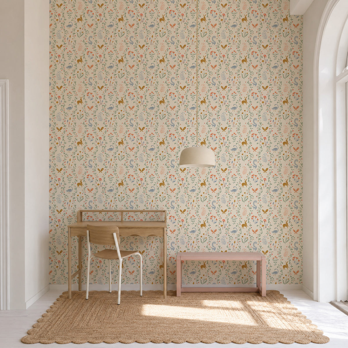 Coles Berry Patch Wallpaper featuring a whimsical pattern of stylized deer, birds, and botanical elements on a cream background, installed on a wall behind a wooden desk and a pink bench.