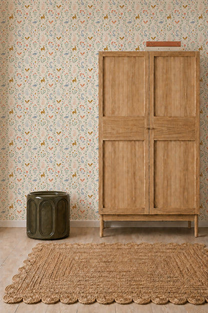 Coles Berry Patch Wallpaper with a whimsical pattern of small deer, birds, and flowers in soft muted colors, displayed behind a wooden wardrobe, a dark green stool, and a woven rug.