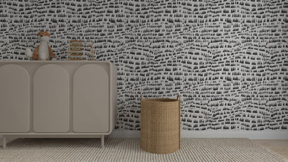 A nursery with a gray dresser holding a stuffed fox and childrens books, a woven basket, textured rug, and black-and-white Daphne Drops Wallpaper Repeat Pattern | Charcoal featuring abstract rows of small trees.