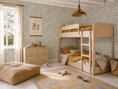 A cozy kids’ bedroom features light wood bunk beds, mustard yellow bedding, a patterned rug, pouf, dresser, and playful Daphne Drops Wallpaper in Olive. Sunlight streams through sheer curtains for a warm, inviting vibe.