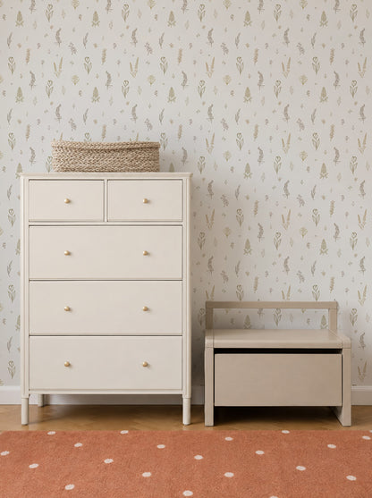 A white dresser and a matching storage bench sit against a wall adorned with Delicate Meadows Wallpaper Sample, showcasing its vibrant color and premium quality, with a woven basket on top. The floor features an orange rug with white polka dots.