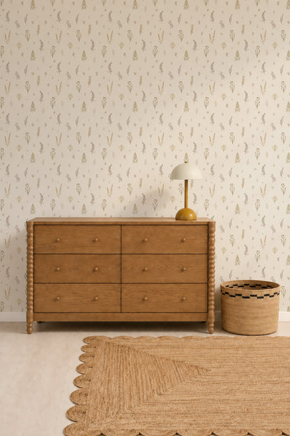 A wooden dresser with six drawers stands against a wall adorned in Delicate Meadows Wallpaper, showcasing its vibrant colour. A yellow lamp and woven basket sit beside it, while a tan textured rug covers part of the light wood floor.
