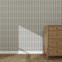A wooden dresser stands on a woven rug beside a wall featuring the Little Abacus Stripe Denim Wallpaper sample. Sunlight casts a diagonal shadow, highlighting the wallpaper’s quality and vibrant blue striped pattern.