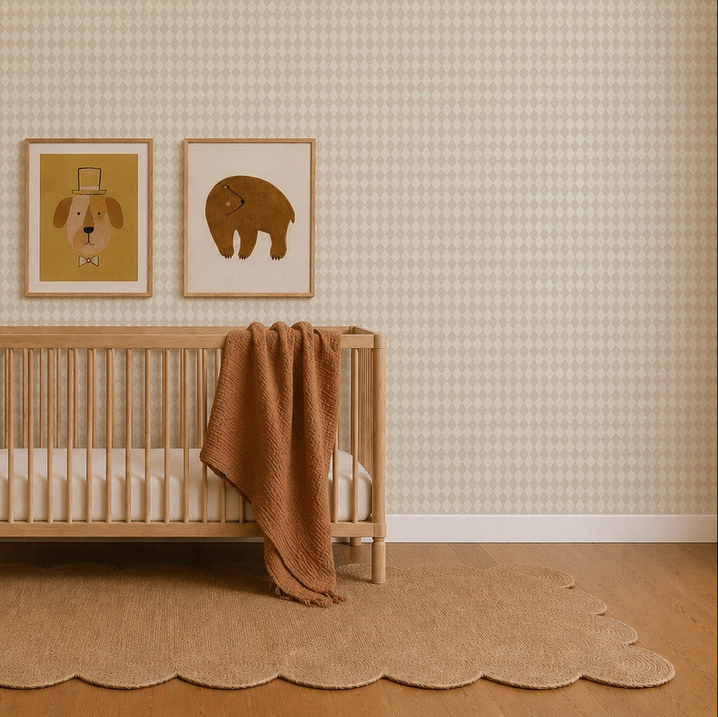 Minimalist nursery featuring a wooden crib, a brown blanket draped over its rail, and a tan scalloped rug. Two animal art prints hang on the wall adorned with Diamond Dancer Wallpaper in Cream, which showcases a subtle beige diamond pattern. The space is finished with light wood floors.