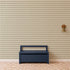 A navy blue bench sits against a wall adorned with Diamond Dancer Wallpaper in green, featuring a geometric diamond pattern; a brass wall sconce is mounted to the right, and a geometric patterned rug is on the floor.