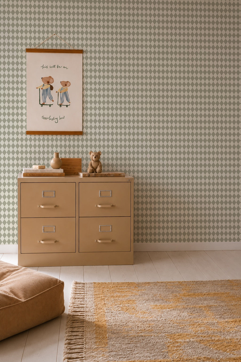 A beige dresser with four drawers sits against a wall covered in Diamond Dancer Wallpaper, Green. On top are decorative items and a teddy bear. Above is a framed art print. A tan rug and cushion are on the light wood floor.