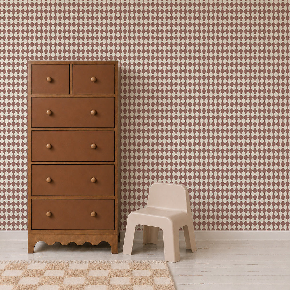 A brown wooden dresser with six drawers stands next to a small beige plastic chair. The background features Diamond Dancer Wallpaper in the Stone Rose colorway, showcasing retro harlequin patterns in shades of brown and cream. A beige rug lies on the light wood floor.