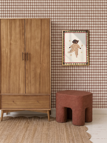 A mid-century wooden wardrobe, a brown textured stool, and a framed illustration of a bear in a circus outfit are displayed against Diamond Dancer Wallpaper in Stone Rose above a light rug.