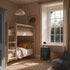 A cozy bedroom with a wooden bunk bed, neutral bedding, Diamond Dancer Wallpaper in Stone Rose, a window with beige curtains, a small black nightstand, bean bag chair, wicker basket, and framed elephant picture on the wall.