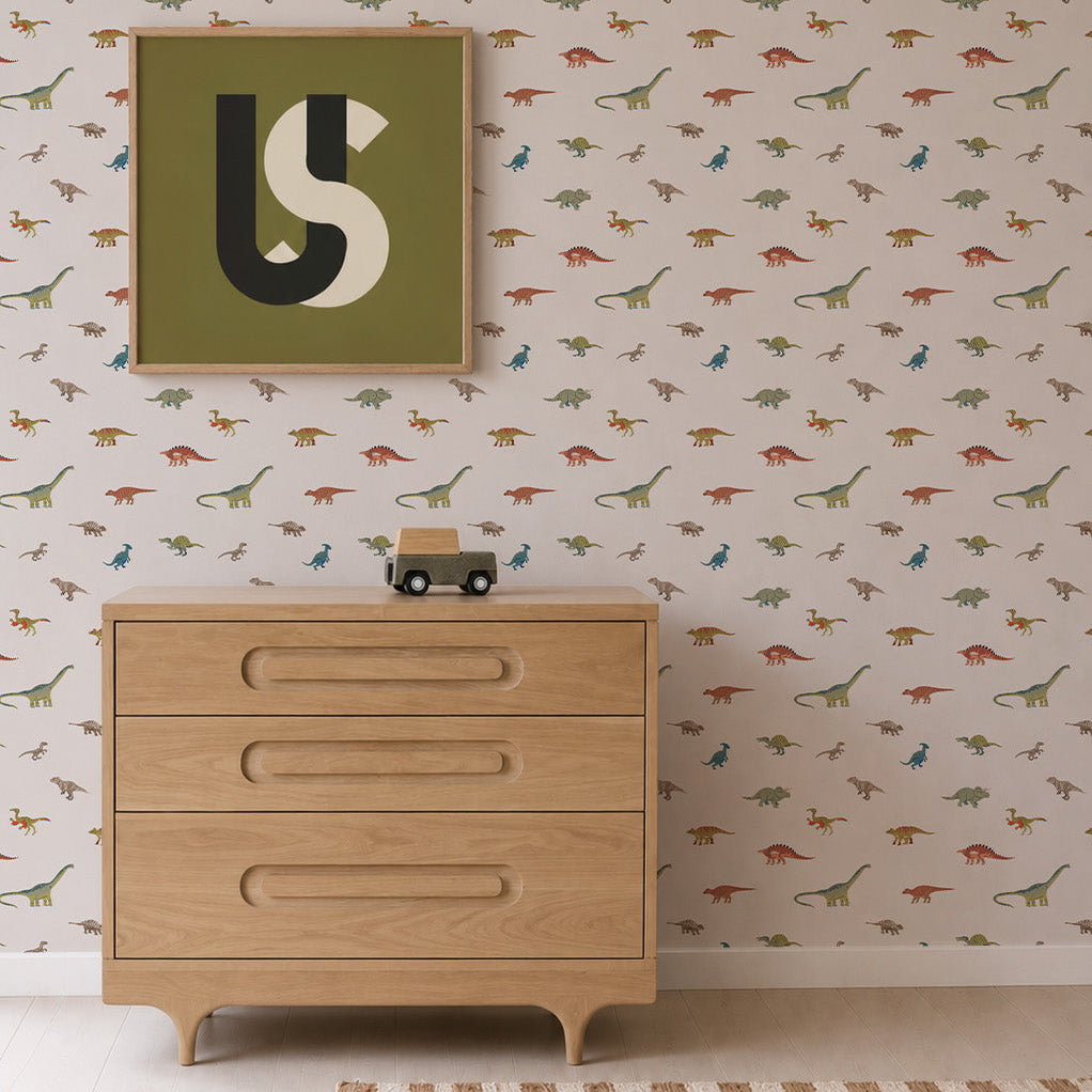 Light wooden dresser with three drawers, a small toy car on top, Dino Discovery Wallpaper featuring playful dinosaurs for young adventurers, and a framed abstract art piece with letters U and S on the wall above.