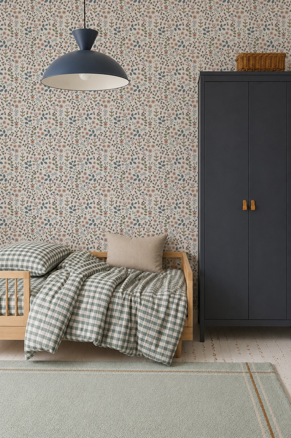 A child’s bedroom featuring a small wooden bed dressed in green plaid bedding and a beige pillow, a dark wardrobe with brass handles topped with a basket, and the whimsical Ditsy Blooms Wallpaper by Sanderson creating an enchanting backdrop. A pendant lamp is suspended from the ceiling.