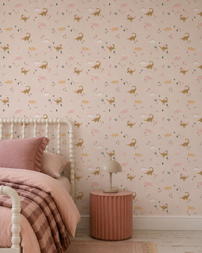 A cozy bedroom with a bed in pink linens, a round pink nightstand with a beige lamp, and playful Dixie Dinosaur Wallpaper featuring deer and florals on a light pink background.