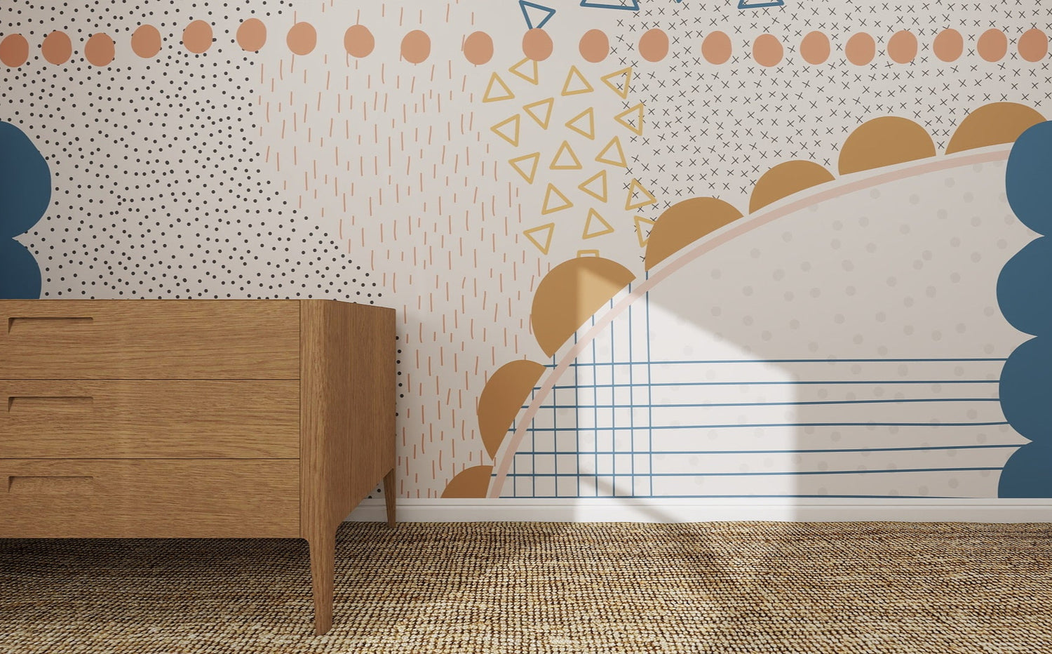 A wooden dresser stands on a woven rug before a wall adorned with the Evie Abstract Wallpaper Mural, featuring blue, mustard, and beige dots, triangles, scallops, and lines. Sunlight highlights this colorful setting.