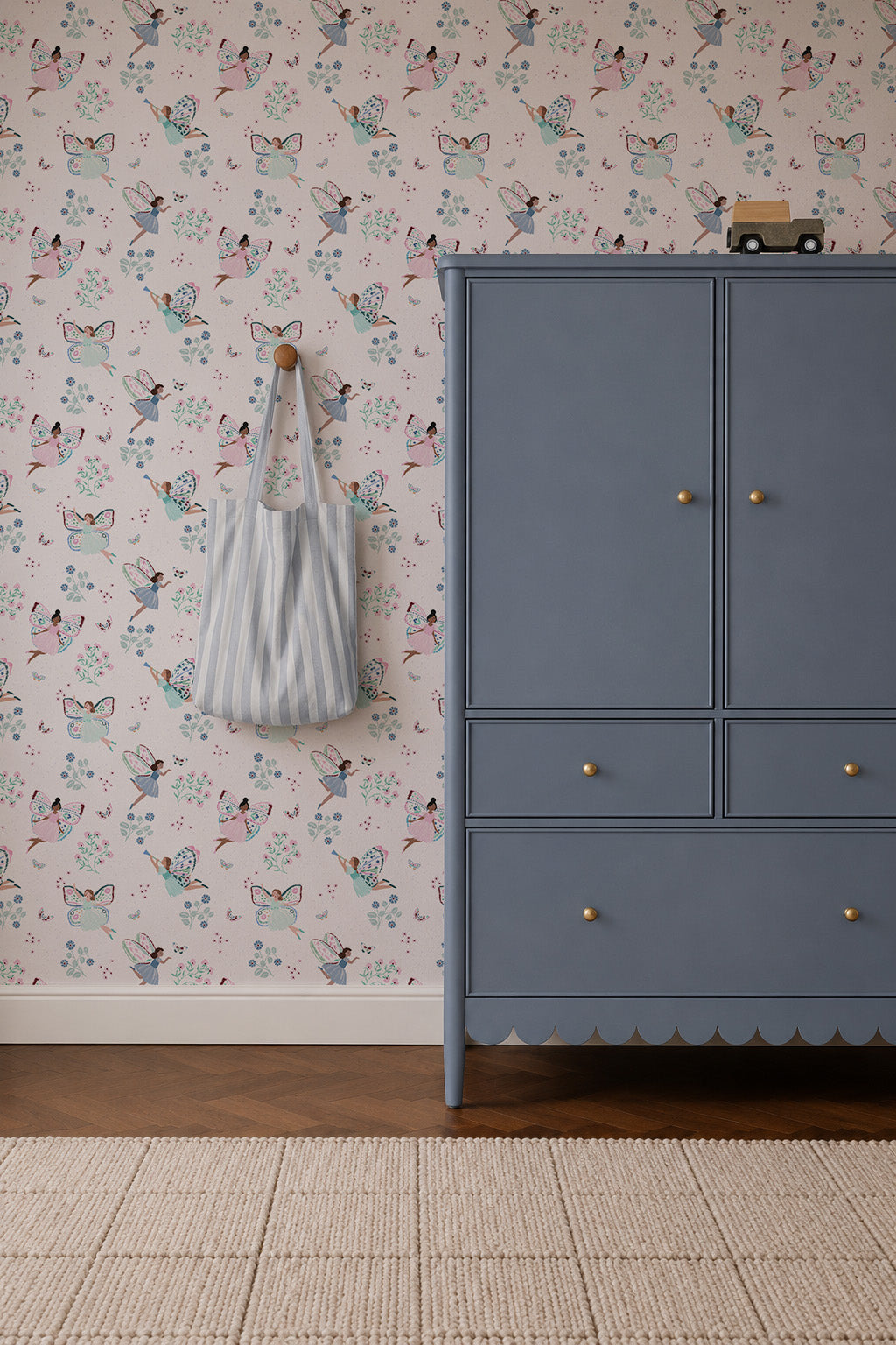 A blue dresser with gold knobs sits on a tan rug. A gray and white striped bag hangs on the wall, which is decorated with Fairy Wonderland Purple Wallpaper featuring playful floral designs.