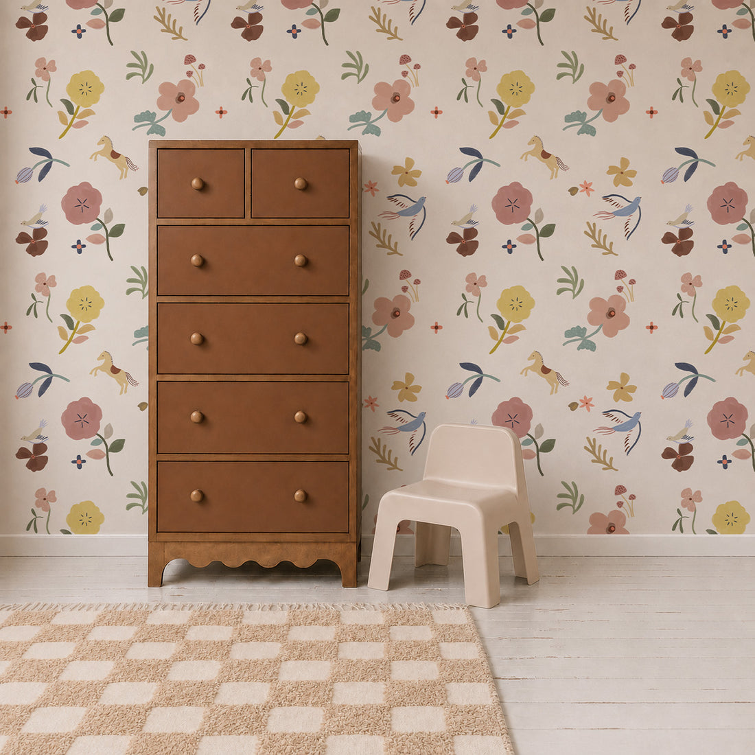 A tall brown dresser and a small beige chair sit on a light wood floor next to a checkered rug. The wall behind them is adorned with Flora &amp; Fable Wallpaper, whose colorful floral pattern brings charm and playful whimsy to the space.