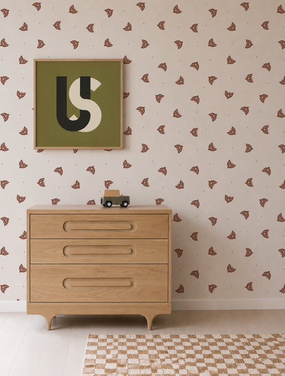A wooden dresser stands against a wall adorned with Flutter Sky Wallpaper Mocha and is complemented by a framed abstract art piece. A small toy car sits on top of the dresser, while a checkered rug covers the floor.