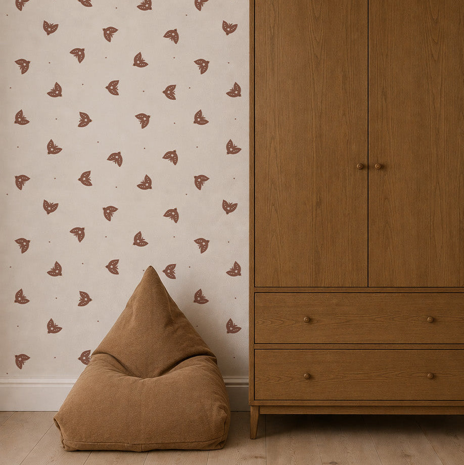 A minimalist room featuring a light wood wardrobe, a brown bean bag chair, and neutral walls adorned with Flutter Sky Wallpaper Mocha—a repeating pattern of small brown butterflies on a beige background. Light wood flooring completes the space.