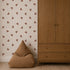 A minimalist room featuring a light wood wardrobe, a brown bean bag chair, and neutral walls adorned with Flutter Sky Wallpaper Mocha—a repeating pattern of small brown butterflies on a beige background. Light wood flooring completes the space.