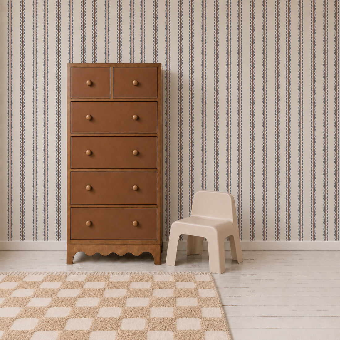 A brown wooden dresser stands next to a small beige plastic chair on a white floor, with a checkered rug and Folk Scallop Stripe Wallpaper in Chambray &amp; Mocha in the background.