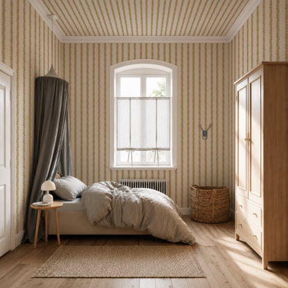 Cozy bedroom featuring the Folk Scallop Stripe Wallpaper in Ochre &amp; Mocha, a bed with gray bedding, a wooden wardrobe, a wicker basket, and a window with sheer curtains. A bedside table with a lamp and a neutral rug are also visible.
