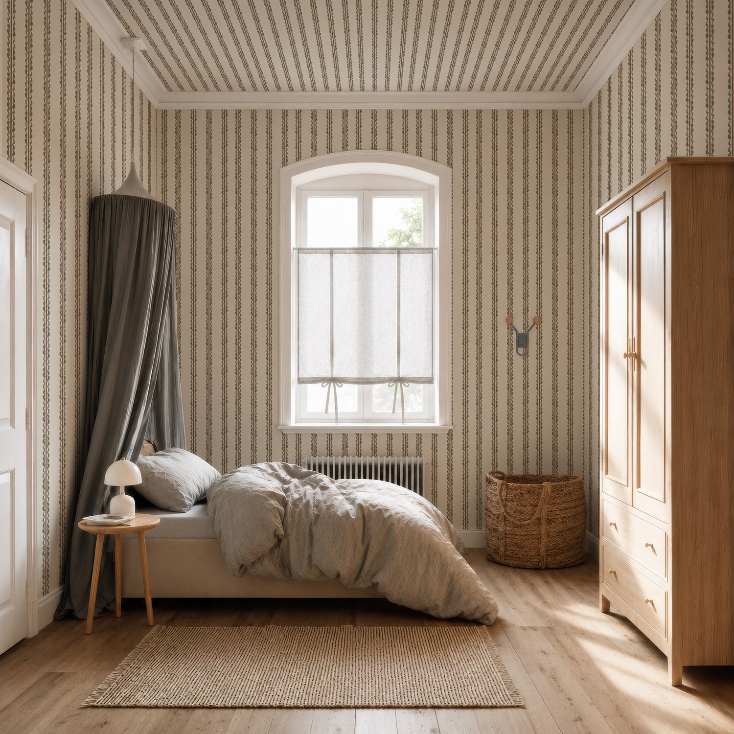 A cozy bedroom features a bed with a gray canopy, wood furniture, and a wicker basket. Sunlight streams through a window adorned with sheer curtains, highlighting the Folk Scallop Stripe Wallpaper in Olive &amp; Mocha. Neutral tones throughout the space create a calm, inviting atmosphere.