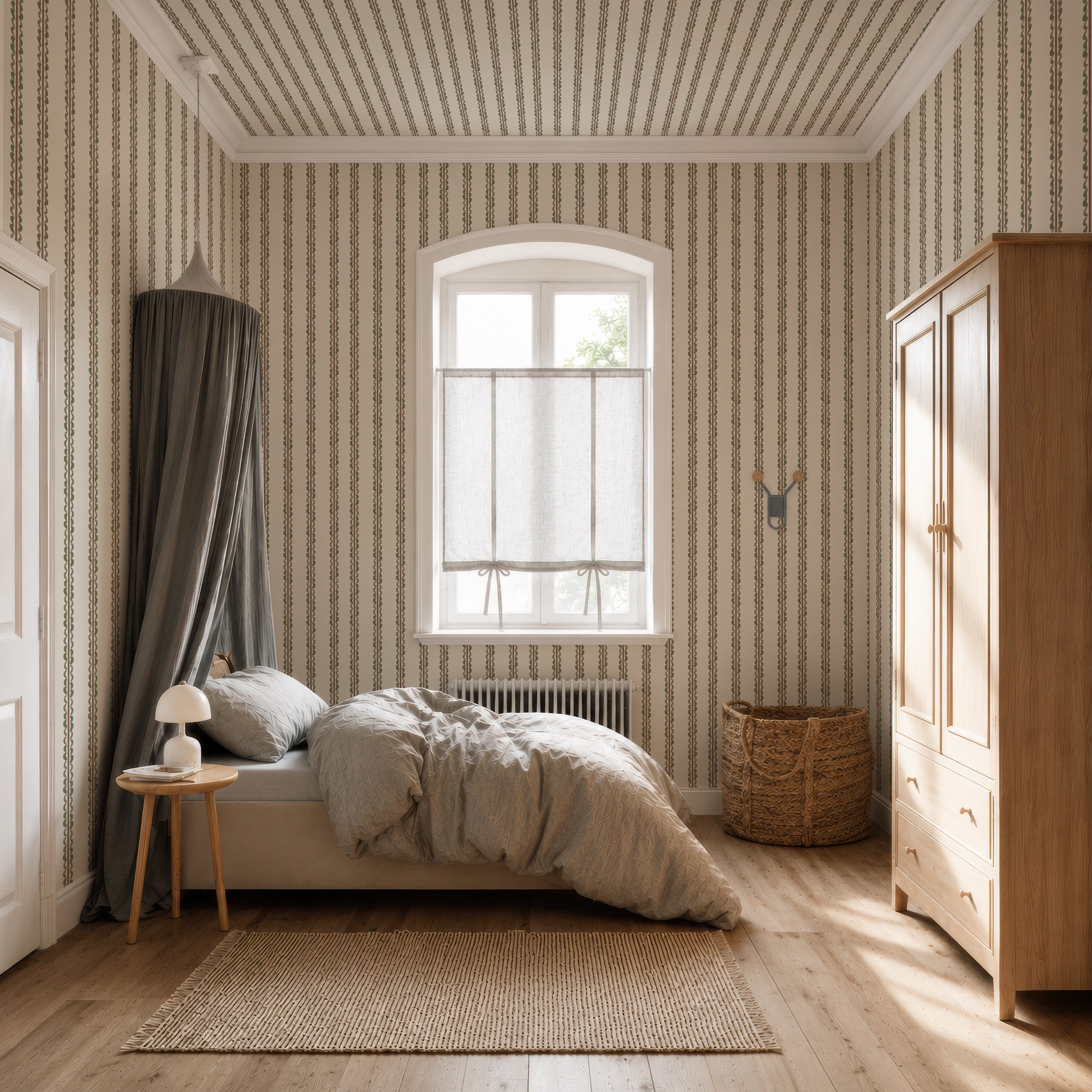 A cozy bedroom features a bed with a gray canopy, wood furniture, and a wicker basket. Sunlight streams through a window adorned with sheer curtains, highlighting the Folk Scallop Stripe Wallpaper in Olive &amp; Mocha. Neutral tones throughout the space create a calm, inviting atmosphere.
