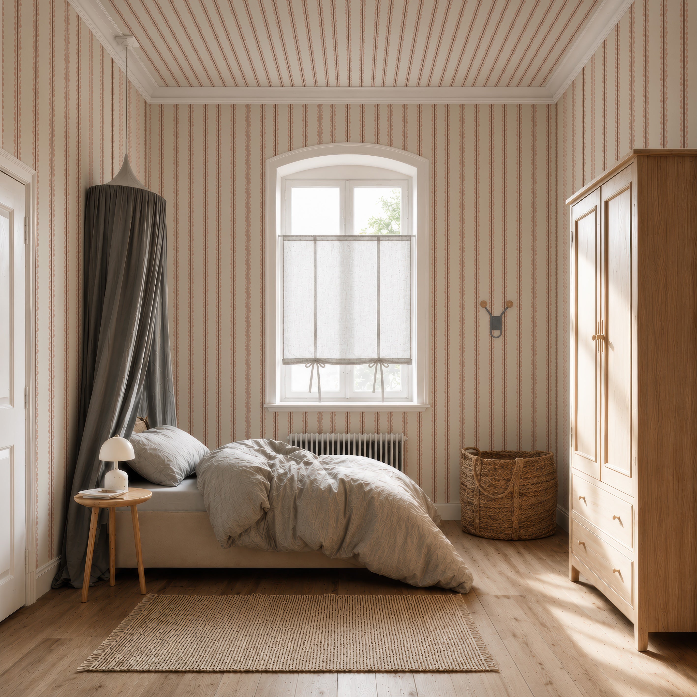 A cozy bedroom featuring the Folk Scallop Stripe Wallpaper in Rose &amp; Mocha, a bed with gray bedding and canopy, a wooden wardrobe, a small side table with a lamp, a woven basket, and a window adorned with sheer curtains that let in natural light.