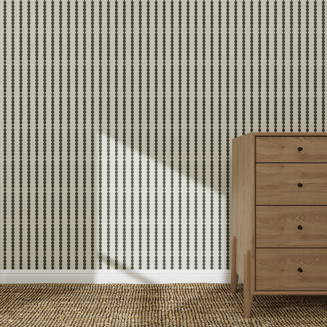 The Little Abacus Stripe Forest wallpaper features bold black dotted stripes behind a wooden four-drawer dresser on a woven rug, with sunlight casting gentle shadows for a serene nursery atmosphere.