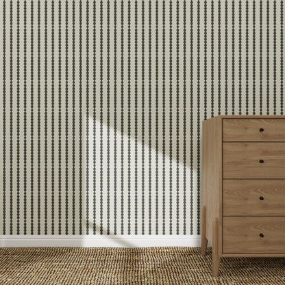 The Little Abacus Stripe Forest wallpaper features bold black dotted stripes behind a wooden four-drawer dresser on a woven rug, with sunlight casting gentle shadows for a serene nursery atmosphere.