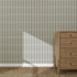 The Little Abacus Stripe Forest wallpaper features bold black dotted stripes behind a wooden four-drawer dresser on a woven rug, with sunlight casting gentle shadows for a serene nursery atmosphere.
