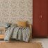 A cozy bedroom with a wooden bed, green plaid bedding, a mustard pillow, a red wardrobe, Forest Floor Wallpaper, white wood floors, and a woven rug.