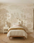 A cozy bedroom features a single bed with neutral bedding and layered pillows. A round jute rug warms the wooden floor, while the wall displays the Forest Hideaway Mural, Neutral—a nature-inspired wallpaper scene.