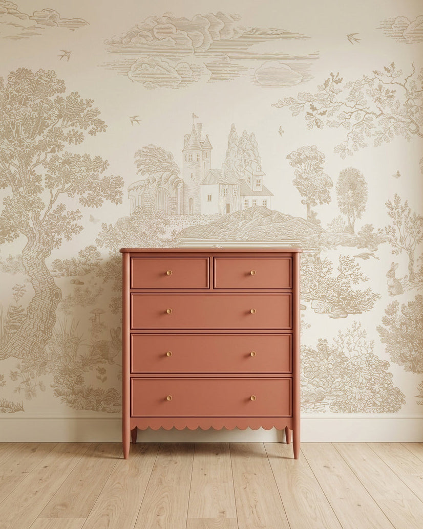 A terracotta-colored dresser with five drawers and gold knobs stands on a light wooden floor against the Forest Hideaway Mural, Neutral, which features a detailed countryside scene with trees, birds, and a house.