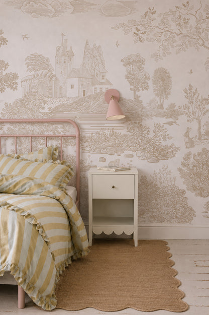 Cozy bedroom with a striped yellow ruffled bedspread, pink metal bed frame, white nightstand, pink wall lamp, jute rug, and the Forest Hideaway Mural in Neutral featuring a scenic castle and nature illustration in soft beige tones.