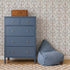 A blue dresser with silver knobs stands next to a blue bean bag chair. A wicker basket sits on the dresser, while Forest Tales Wallpaper with whimsical floral patterns decorates the background above a checkered rug on a wooden floor.