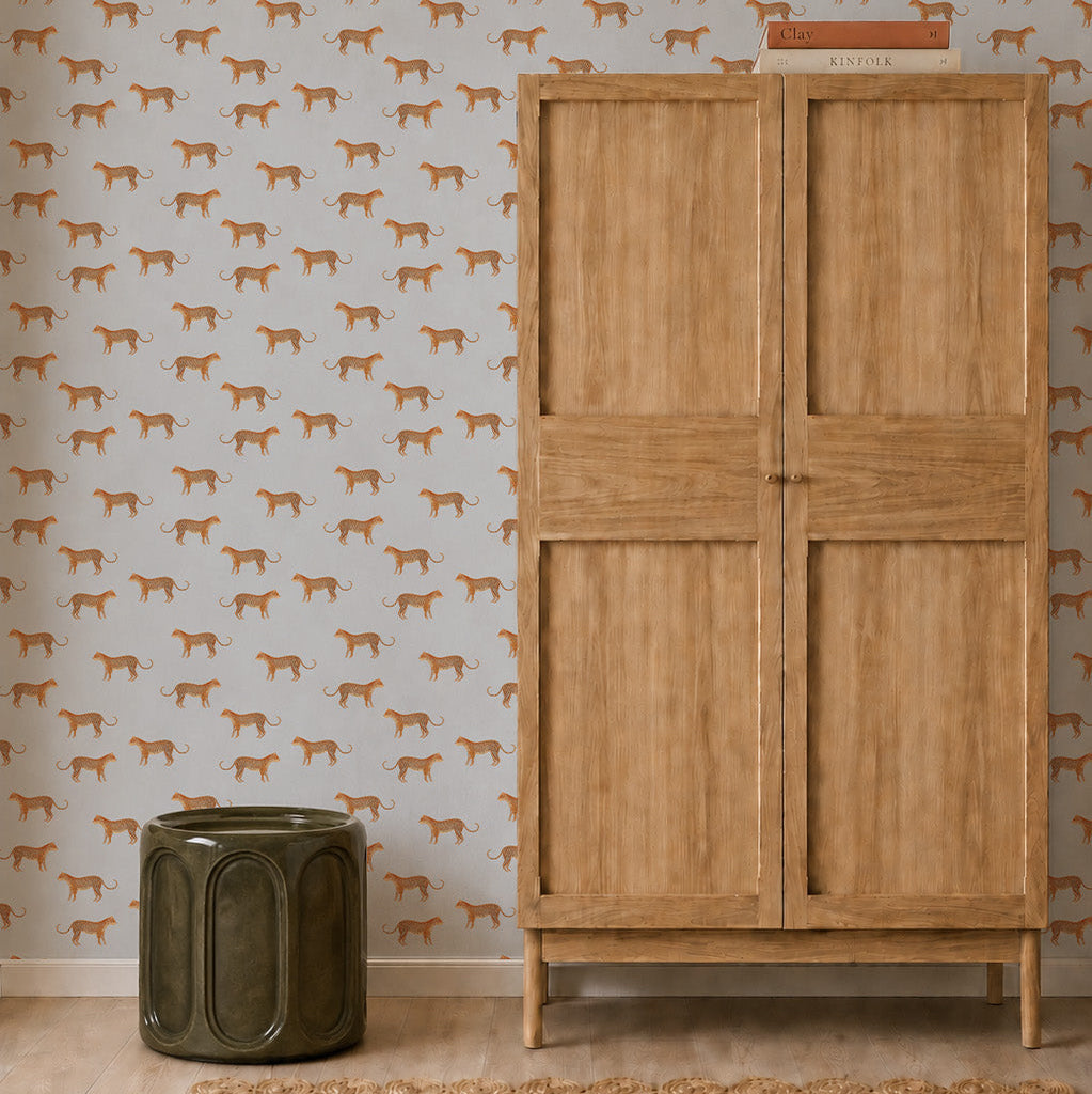 A light wooden wardrobe stands next to a green ceramic stool. The wall behind them is decorated with Goldies Cheetah Wallpaper in blue, featuring a repeating animal print pattern.