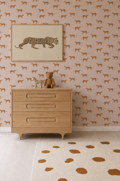 A dresser with a zebra and teddy bear sits below a framed cheetah print on a wall covered in Goldies Cheetah Wallpaper, Pink. A beige rug with brown spots is on the light wood floor.